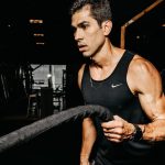 A determined male athlete working out with battle ropes in a dimly lit gym, showcasing strength and fitness.
